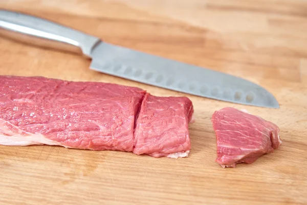Raw meat slices cutted with knife on wooden board Stock Photo