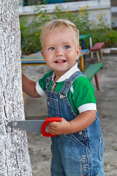 Father rolls young son in a wheelbarrow with garden tools in the backyard of his house. A man with a beard farmer put the baby in a wheelbarrow with tools. Little Helper on the farm with a bearded father — Stock Photo, Image