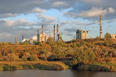 The plants on the banks of the picturesque river surrounded by autumn forest. Factory pipe smoke and pollute the environment clipart