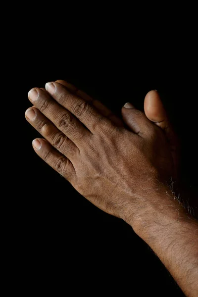 Praying hands of Indian Catholic man isolated on a black background.