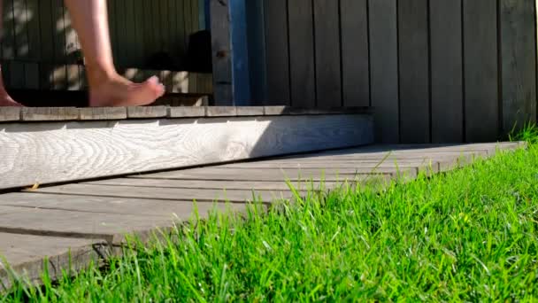 Meisjes voeten met rode nagels lopen op een weelderig gras. Een vrouw loopt blootsvoets door een groen gazon. Vrouwelijke afstammeling van de houten trap. Gezonde procedures. Dichtbij schot. Vrijheid en genieten van het leven. Stockvideo's