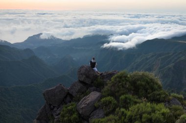 Dağın tepesinde yürüyüş yapan genç bir adamın görüntüsü.