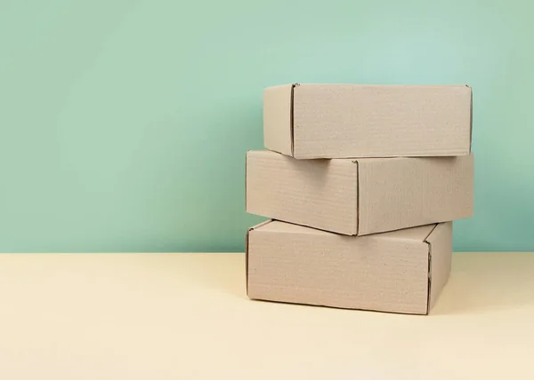 Stack of Brown cardboard boxes on mint background. Blank carton box. Gifts packaging concept. Craft box for gift or present on neutral backdrop. Shopping. Copy space.