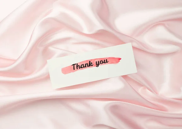 Thank-you note with Thank You inscription on pastel pink silk background: the concept of manifestation of gratitude and appreciation. Flat lay