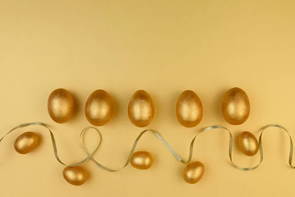 Декоративные деревянные пасхальные яйца раскрашены золотом на желто-золотом фоне. Поздравительная открытка. — стоковое фото
