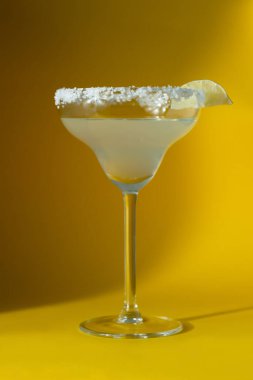 Bir bardak tuzlu margarita ve sarı arka planda bir dilim limon. Ulusal margarita günü konsepti.