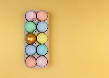 Çok renkli ahşap dekoratif paskalya yumurtaları karton ambalajda sarı arka planda. Mutlu Paskalya tebrik kartları. Boşluğu kopyala.