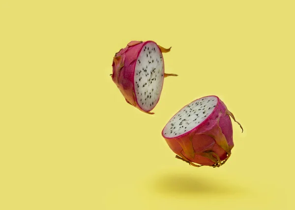 Two halves of a dragon fruit with white flesh levitate against a yellow background. The pink pitaya fruit is low in calories, rich in essential vitamins and minerals, and contains dietary fiber. Copy