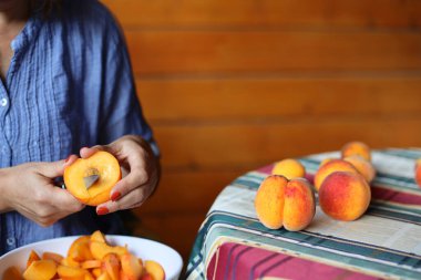 Kadın elleri şeftali reçeli yapmak için taze şeftali kesiyor. Bir kadın ahşap bir terasta oturuyor. Kır Evi Estetiği.