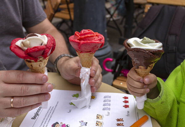 Три руки держат разноцветные мороженое Gelato мороженое конусы. Розовые скопс в красном, розовом и шоколадном вкусах. Будапешт, Венгрия