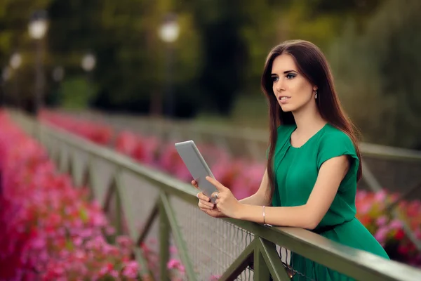 Frau mit digitalem Tablet auf einer Brücke mit Blumen — Stockfoto