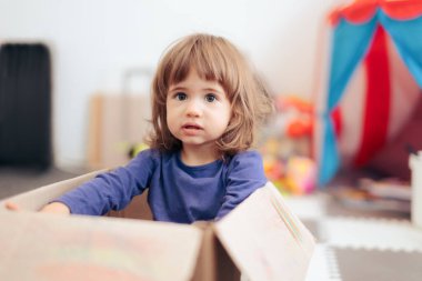 Evde karton bir kutuda oynayan küçük kız.