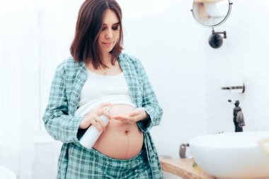 Hamile kadın banyoda karnına losyon sürüyor.