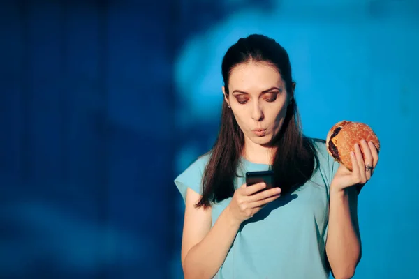 Woman Checking Smartphone Her Lunch Break Holding Burger — Stok Foto