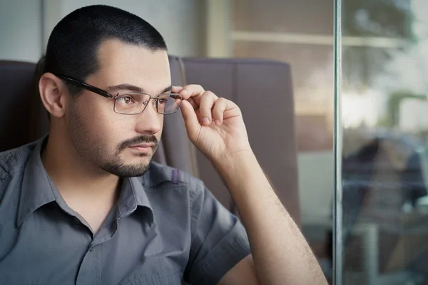 Joven con gafas mirando por una ventana — Foto de Stock