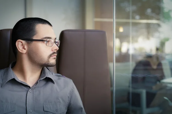 Jeune homme portant des lunettes regardant par la fenêtre — Photo