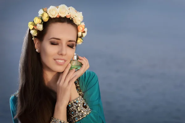 Mulher nova com grinalda floral segurando garrafa de perfume na paisagem costeira — Fotografia de Stock