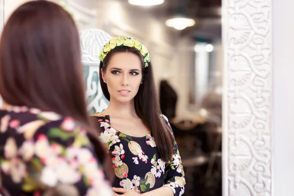 Hermosa chica mirando en el espejo y probándose el vestido floral — Foto de Stock