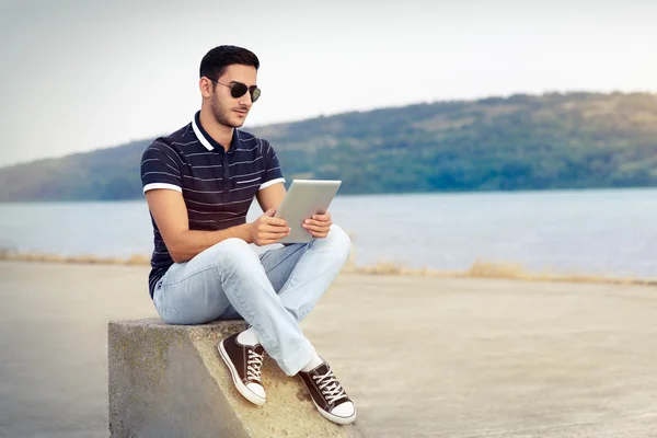 Jovem com óculos de sol e Tablet à beira da água — Fotografia de Stock