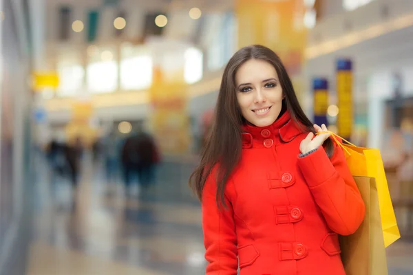 Счастливая девушка в красном пальто за покупками в магазине — стоковое фото
