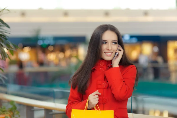 Köpcentret flicka i en röd kappa pratar på Smartphone — Stockfoto