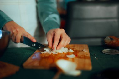 Ev hanımı doğrama tahtasındaki soğanı kesmek için bıçak kullanıyor.