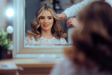 Kuaför müşterisinin dalgalı kıvırcık saçlarını tarıyor.