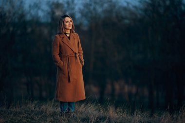 Uzun kahverengi bir ceket giyen güzel, modaya uygun bir bayan.