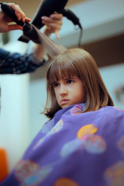Üzgün küçük kız kuaförde sıkılıyor, saçını kestiriyor.