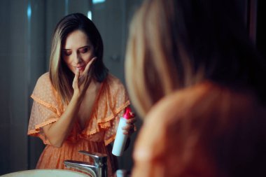 Güzel bir kadın banyo aynasında kavanozdan nemlendirici krem sürüyor.