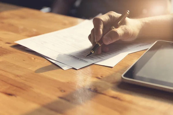 La main de l'homme signant formulaire de demande avec tablette sur table en bois — Photo
