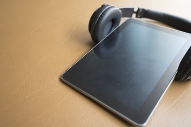 kulaklık ve kahverengi deri yastık üzerinde dijital tablet