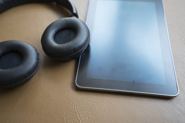 kulaklık ve kahverengi deri yastık üzerinde dijital tablet