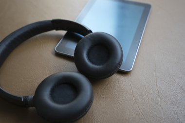 kulaklık ve kahverengi deri yastık üzerinde dijital tablet