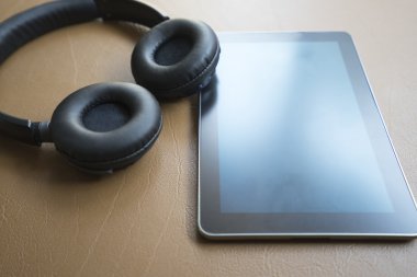 kulaklık ve kahverengi deri yastık üzerinde dijital tablet