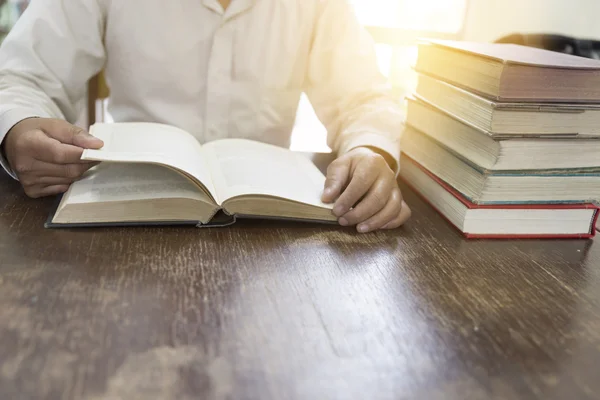 Mann liest Buch mit Lehrbuchstapel auf Holztisch — Stockfoto