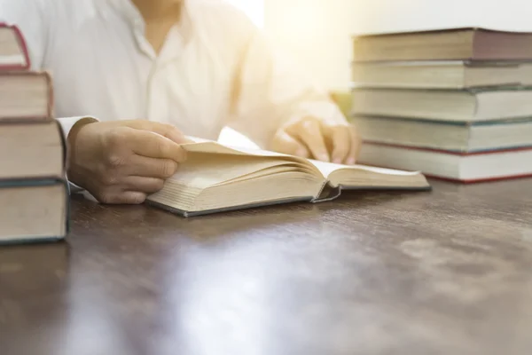Mann liest Buch mit Lehrbuchstapel auf Holztisch — Stockfoto