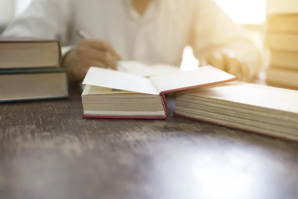 Mann liest Buch mit Lehrbuchstapel auf Holztisch — Stockfoto