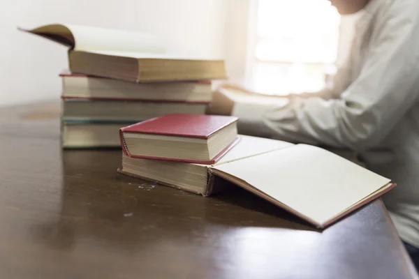 Mann liest Buch mit Lehrbuchstapel auf Holztisch — Stockfoto