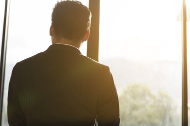 Ofis penceresinden bakan takım elbiseli bir iş adamı.