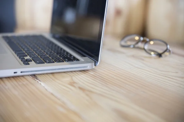 Óculos com notebook de computador portátil em mesa de madeira — Fotografia de Stock