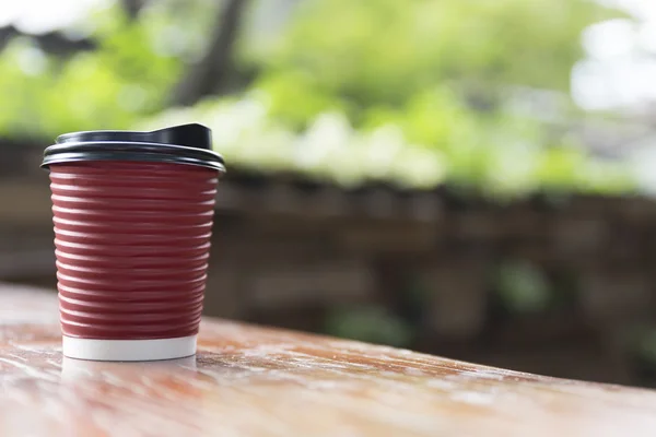 Kaffeetasse aus rotem Papier auf Holztisch mit grünem Blätterhintergrund — Stockfoto