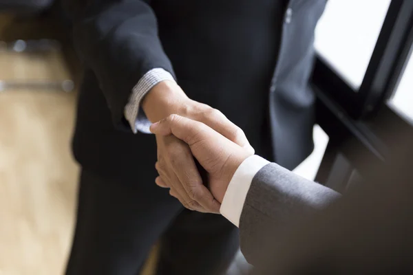 Affärsmän i kostym skakar hand bredvid fönstret - business teamw — Stockfoto
