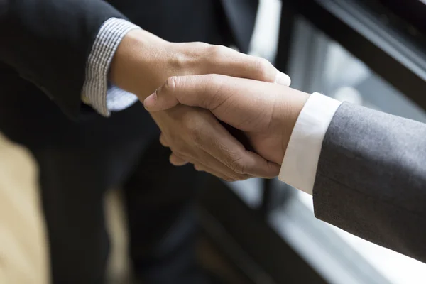 Affärsmän i kostym skakar hand bredvid fönstret - business teamw — Stockfoto