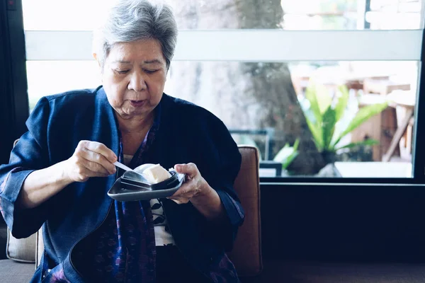 Yaşlı Asyalı yaşlı yaşlı yaşlı kadın restoranda cheesecake yiyor. olgun emeklilik yaşam tarzı
