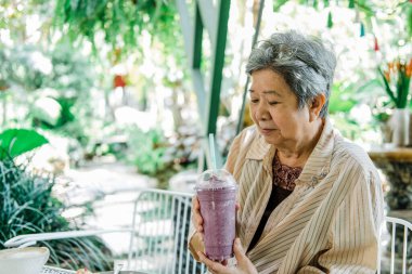 Yaşlı Asyalı yaşlı yaşlı yaşlı kadın restoranda meyveli yoğurt içiyor. olgun emeklilik yaşam tarzı