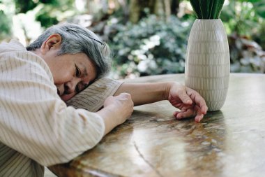 Stresli, bitkin, üzgün, üzgün Asyalı, yaşlı, yaşlı, yaşlı bir kadın bahçede oturuyor..