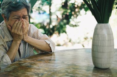 Stresli, bitkin, üzgün, üzgün Asyalı, yaşlı, yaşlı, yaşlı bir kadın bahçede oturuyor..