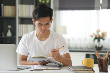 Asyalı genç öğrenci genç girişimci bilgisayar yazma notuyla çalışıyor evde internetten öğrenim görüyor. Webinar toplantısını öğreniyorum. Covid salgınında sosyal uzaklık