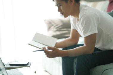 Asyalı genç öğrenci genç girişimci bilgisayarla çalışıyor evde internetten öğrenim görüyor. Webinar toplantısını öğreniyorum. Covid salgınında sosyal uzaklık